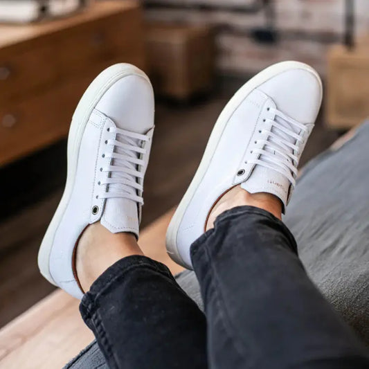 zapatillas blancas de cuero Barefoot de diseño clásico y minimalista, combinadas con pantalones oscuros, en un ambiente interior.